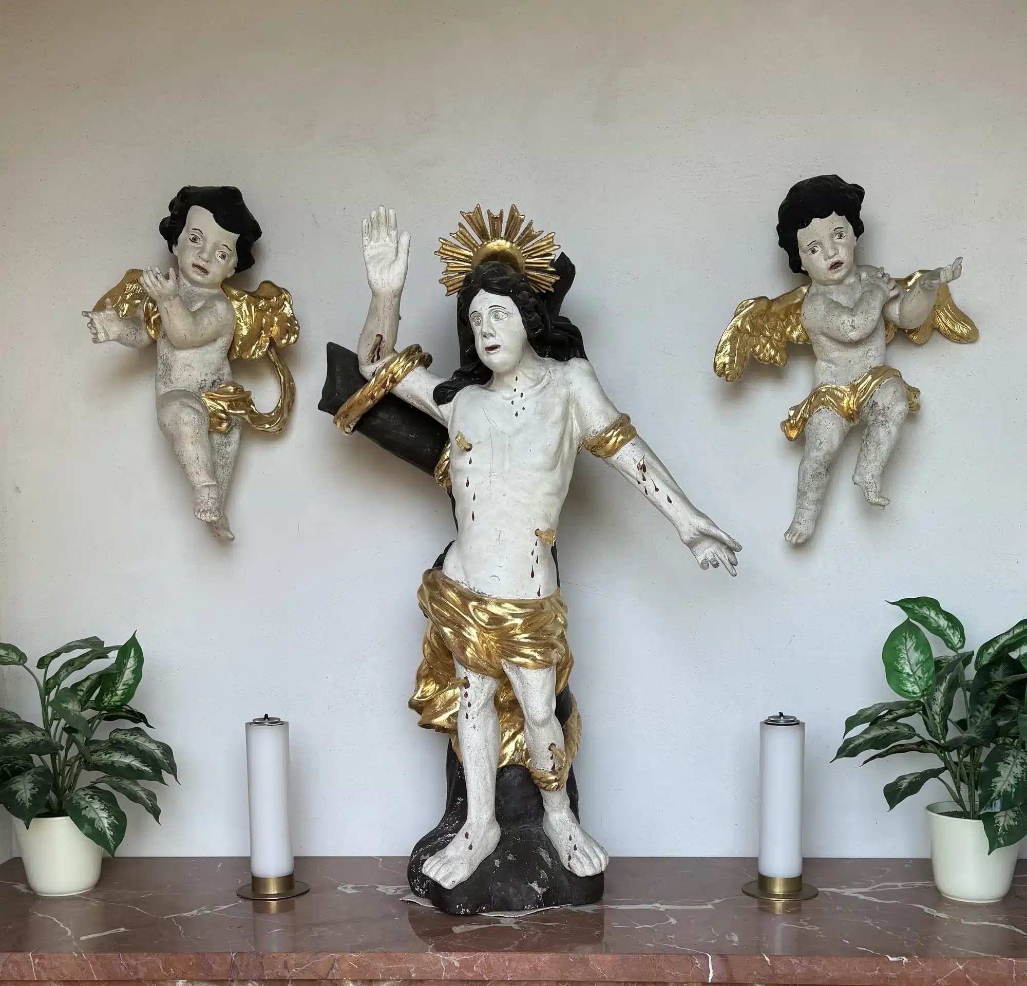 Übermalte, beschädigte Sebastiansfigur mit Engeln auf dem Marmorsockel