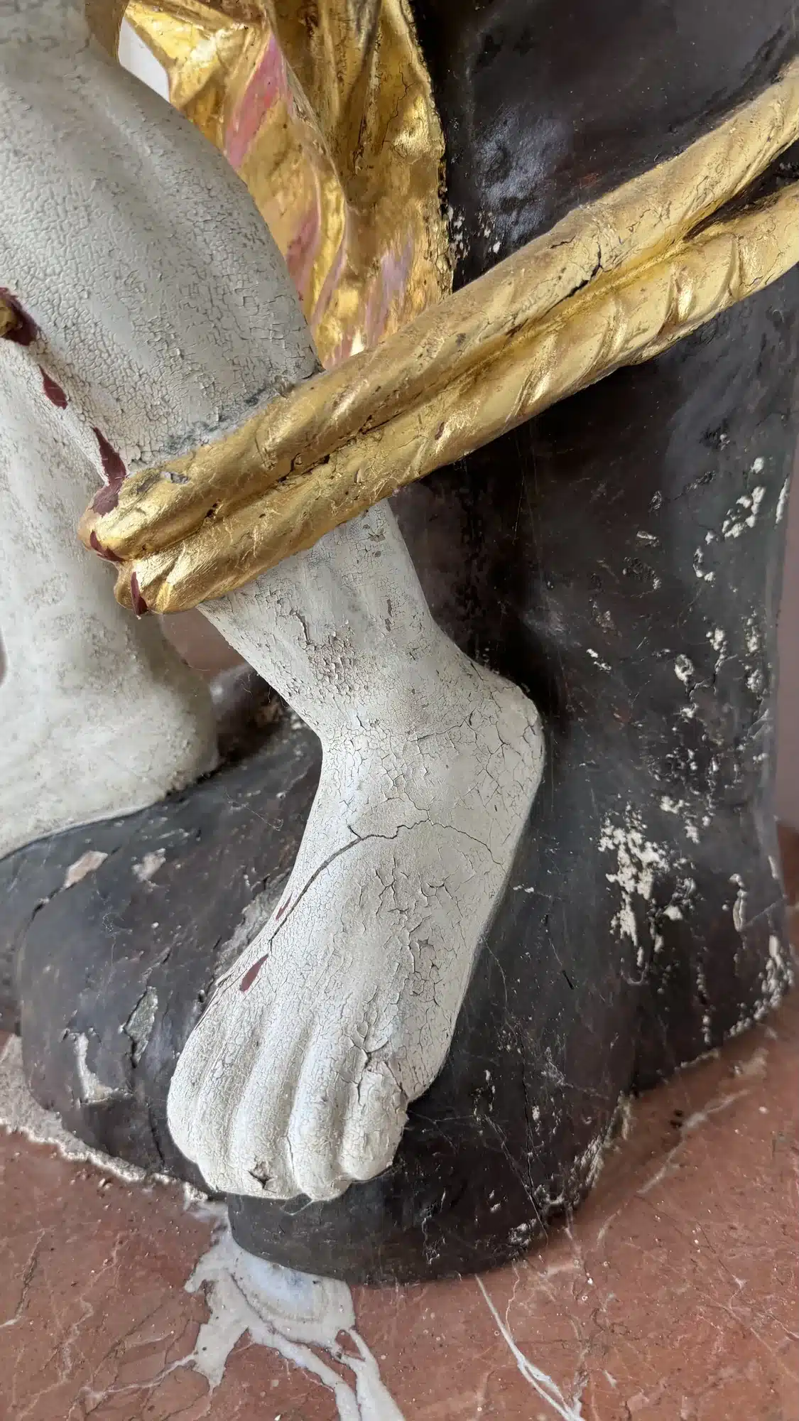 Dicke, rissige Lackschichten an den Füßen der Sebastiansfigur vor dem Entlacken